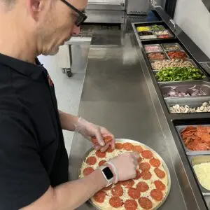 A man in glasses is cutting pepperoni pizza
