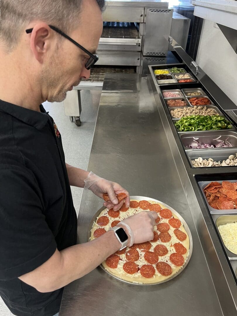 A man in glasses is cutting pepperoni pizza